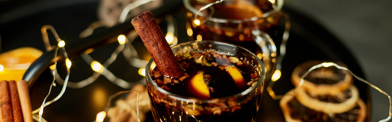 Banner Christmas mulled red wine with spices and oranges on a black table with light garland,...