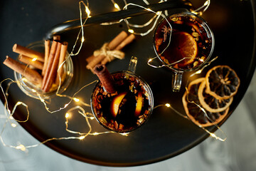 Christmas mulled red wine with spices and oranges on a black table with light garland, traditional...
