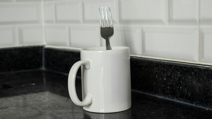 porcelain mug standing on black kitchen counter chrome plated fork in mug
