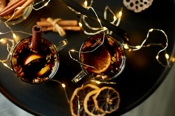 Christmas mulled red wine with spices and oranges on a black table with light garland, traditional hot drink at Christmas, festive cocktail