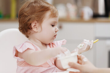 Motherhood and health . Baby's health and healthy food . Mother feeding her baby girl with spoon. Mother giving healthy food to her adorable child at home