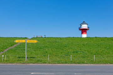 Ein rot-weißer Leuchtturm ragt über einen Deich im Alten Land bei Lühe, Deutschland