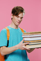 vertical photo of a student in a blue t-shirt with a stack of new books in his hands with his eyes closed