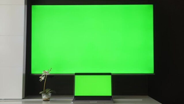 Modern laptop and TV with green screens close up.