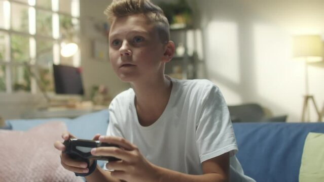 Close up shot of excited teenage boy sitting on couch and playing video game on TV at home