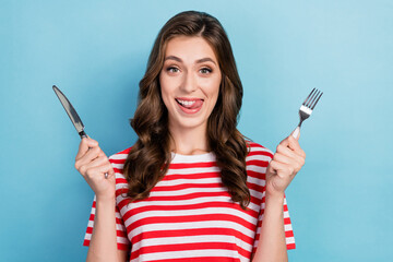 Photo of tricky sweet girl dressed red t-shirt holding knife fork smiling isolated blue color...