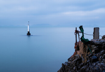 Concrete post in the sea probably for mooring or navigation.  Long exposure gives the sea a smooth surface.
