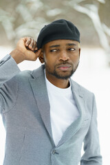 Stylish african man on winter background. Young african in suit and beret posing for camera in snowy park