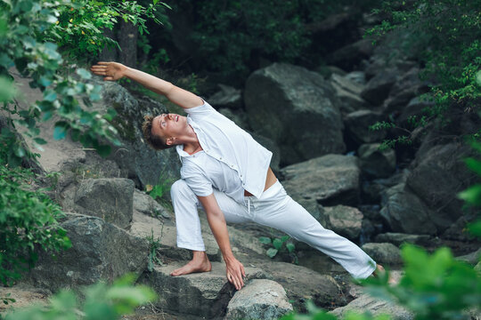 a young guy does yoga in nature among the stones. Utthita Parshvakonasana - the pose of the extended side angle in the practice of yoga Parshva.