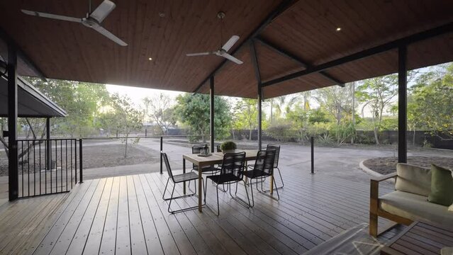 Wooden Deck luxurious outdoor setting with table and couch. Tropic outdoor area and wooden patio roof. Veranda of house in rural area. Green gum trees and garden surrounding