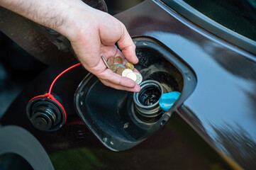 hand of man putting coins in car tank, closeup, expensive fuel concept, fuel crisis