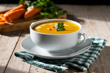 Carrot soup with cream and parsley on wooden table.