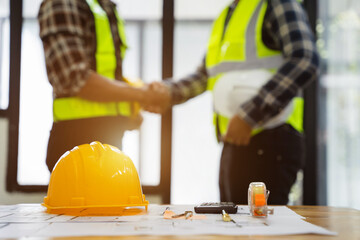 Yellow hard hat on workbench with construction worker hands shaking greeting start plan contracting new project in construction office center and contractor concept.