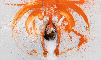 portrait and upper body of young sexy naked pregnant, redhead woman in orange color painted, lies decorative, elegant on the Studio floor, paints big circle with her arms like angel wings