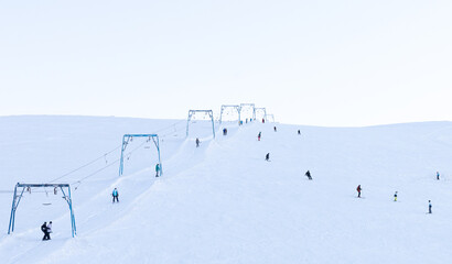 Skiing and snowboarding. A ski slope with a ski lift and small figures of people on a background of white snow