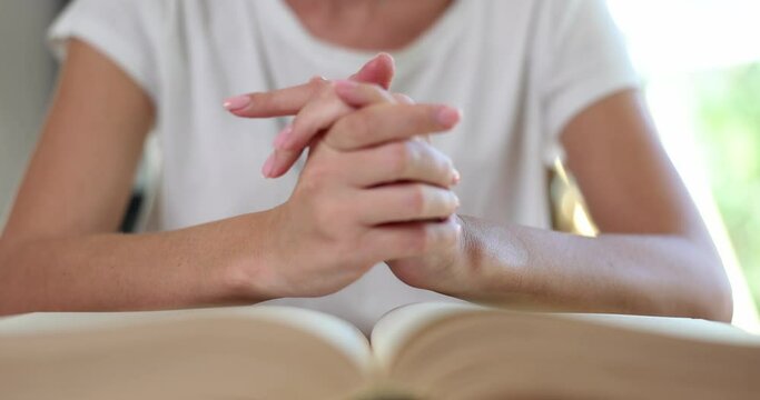 Woman prays with hands clasped on Bible