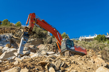 Heavy organge excavator with shovel standing on hill with rocks