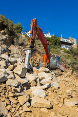Heavy organge excavator with shovel standing on hill with rocks