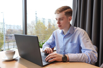 Fototapeta premium A young man works at a laptop at a table in the room. 