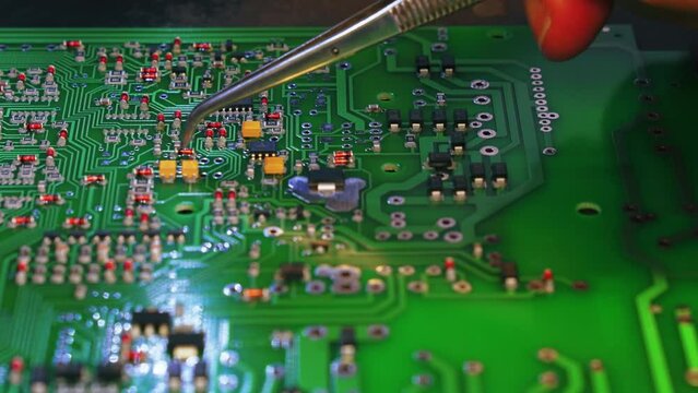 Basic components of modern electric devices. Manual montage of little pieces glued to green printed circuit board. Caucasian specialist using tweezers. High quality 4k footage