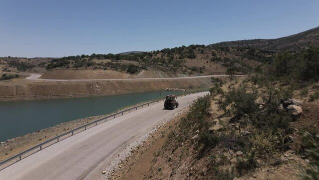 Drone following red trucktor slowly driving a road in turkey karaman between blue lake and mountains at a sunny summer though curves