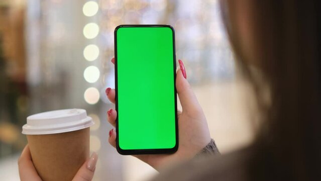 Mall. Shopping center. Department store. Back view of brunette holding chroma key green screen smartphone watching content. Shopping online. Gadgets and contemporary people concept. 4K