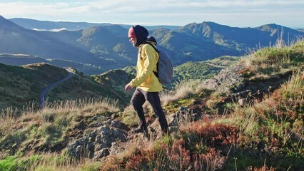 The tourist walks the mountain trail at sunrise, in the background there is a panorama of the mountain range.