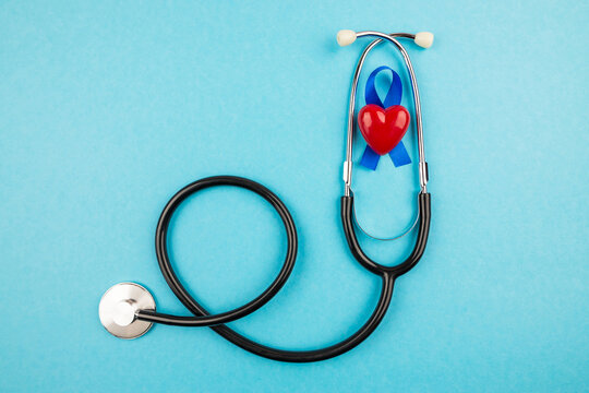 Top view photo of stethoscope and blue ribbon with small red heart, prostate cancer awareness symbol