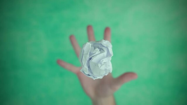 Hand throwing up and catching crumpled white paper ball over bright-colored background in bright studio extreme closeup slow motion