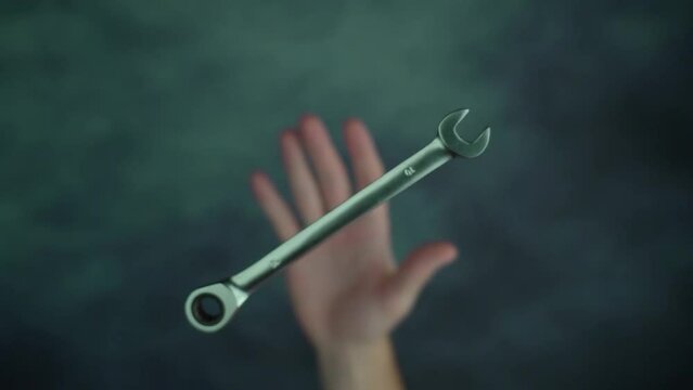 Man hand throws up and catches steel spanner above spotted green table surface at bright studio illumination macro slow motion