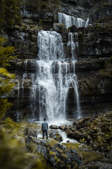 A person standing on top of a rock with the waterfalls of Madonna di Campiglio in the background