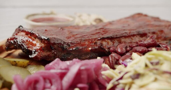 A large Plate that includes Baby Back Ribs with cherry chipotle sauce. cooked slowly on smoker, sauce, BBQ beans, coleslaw, pickled onions, pickled cucumbers, Rotating on isolated white background