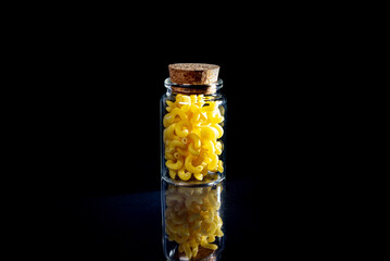 raw pasta in glass jar, wine glass. in bucket. raw pasta on black background. front view raw pasta, dropped from hand, place for text, yellow long spaghetti straws,