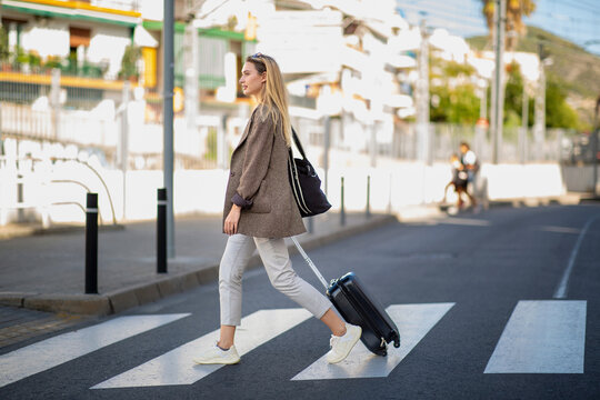 Caucasian woman pulling luggage while crossing city street