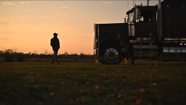 Semi Truck Driver in Front of His Vehicle During Scenic Countryside Sunset. Transportation Industry Theme.