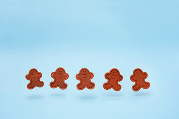 Smiling gingerbread mans made of modeling clay floating and dancing on the blue background. Winter christmas decoration christmas. Minimal creative holiday concept.