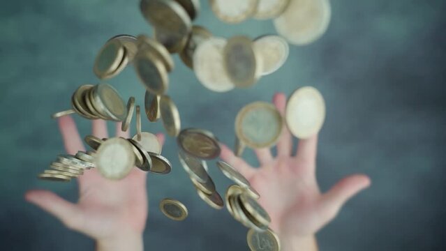 Both hands throwing up handful pile of small steel coins above blurred and spotted green table in bright studio macro slow motion