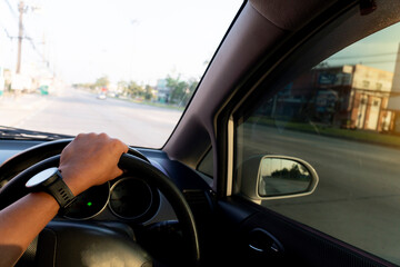 Hand of people hold the steering wheel to the right. Driving inside car on the empty road at day. blurred of town beside road in Thailand.