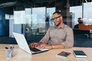 Fototapeta premium African american programmer at work with laptop inside office, man in glasses and casual writing code for programs.