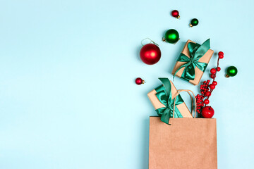 Brown paper shopping bag with Christmas decorations and gifts on blue background.