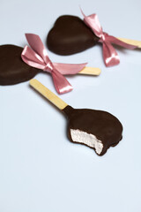 Marshmallows in chocolate on a stick. One bite. zephyr hearts glazed with chocolate. They lie on a white surface.