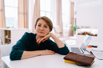 Thoughtful middle aged woman working on laptop at home