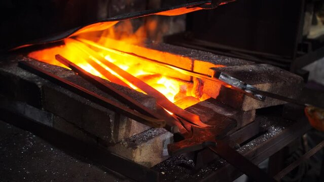 Two blanks of swords are heated in a furnace. The flame heats up the blanks of swords in the forge of the blacksmith's workshop