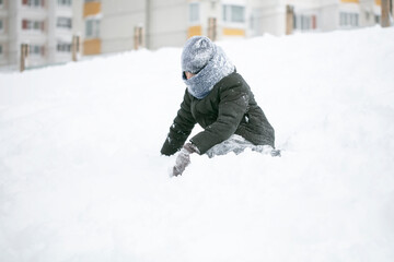 Fototapeta na wymiar A boy warmly dressed plays in the snow on a winter day.