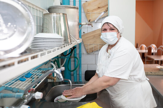 A woman canteen worker washes dishes.