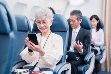 飛行機でスマホを使うシニア女性