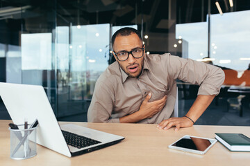 Fototapeta na wymiar heart attack at work, businessman sick has severe chest pain heartache, african american man working inside office building using laptop.