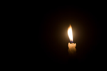 A single burning candle flame or light glowing on a spiral white candle against little blowing wind...
