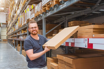 Caucasian young male smiling glasses warehouse worker holds and puts box on shelf against the...
