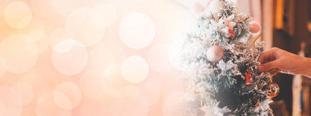 Close up look of Hand is decorated Christmas tree with golden ball. Concept of Celebration Christmas background, postcard, presentation and banner with blur bokeh copyspace background widescreen.